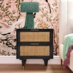 A matte black solid wood bedside table featuring two drawers with natural cane panels and gold-tipped legs - Modera Furnish.