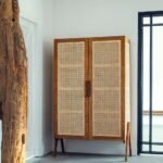 A tall natural wood storage cabinet featuring two hand-woven rattan doors and eight internal shelves - Modera Furnish.