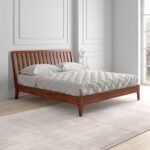 A reddish brown solid wood king size bed with a spindled headboard and tapered legs in a teak finish - Modera Furnish.