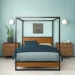 A black industrial carbon steel 4-poster bed frame featuring solid wood headboard panels and a reinforced slat system - Modera Furnish.