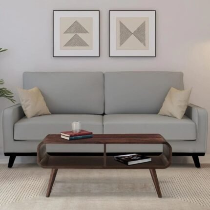 A 35-inch teak-finished solid Sheesham wood coffee table featuring curved waterfall edges, splayed tapered legs, and dual open storage compartments - Modera Furnish.