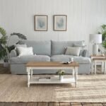 A 110 cm natural and white wooden coffee table featuring an open lower storage shelf, elegant turned legs, and a multi-tonal wood grain top - Modera Furnish.