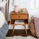 A natural warm brown solid wood bedside table featuring a single drawer with a round knob and an open storage shelf on splayed legs - Modera Furnish.