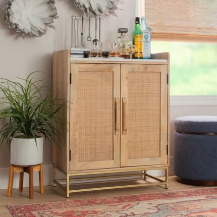 A natural wood bar cabinet featuring two cane-panel doors, a white marble top, and a gold metal base - Modera Furnish.