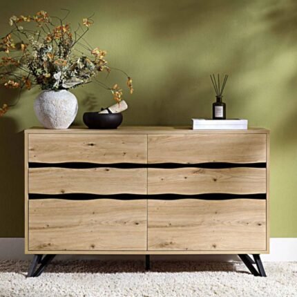 A light oak effect six-drawer chest of drawers featuring wave-cut handles and angled black metal legs - Modera Furnish.