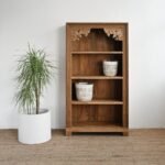 A natural hand carved solid wood bookshelf featuring three open shelves and an intricate floral-patterned archway - Modera Furnish.