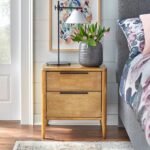 A warm brown solid wood bedside table featuring two drawers with sleek black handles and a hand-stained finish - Modera Furnish.