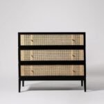A black solid acacia chest of drawers featuring three hand-woven rattan drawer fronts and polished brass hardware - Modera Furnish.